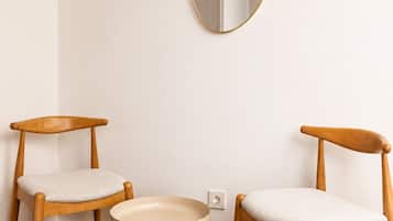 A room with two wooden chairs, a round table, and a wall-mounted oval mirror.