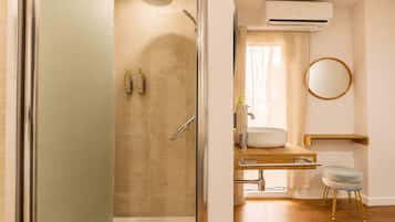 Un baño moderno con cabina de ducha de vidrio, un lavamanos con espejo y un equipo de aire acondicionado.