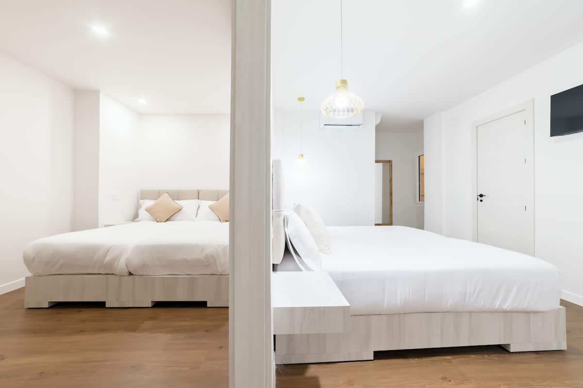 A modern bedroom with two beds, a wooden floor, and a white color scheme.
