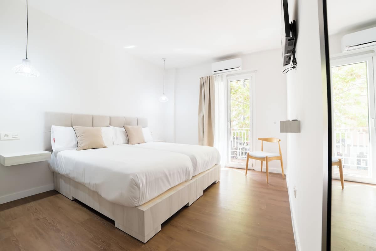 A modern bedroom with a large bed, a bedside table, a chair, and a view of the outdoors through a sliding door.