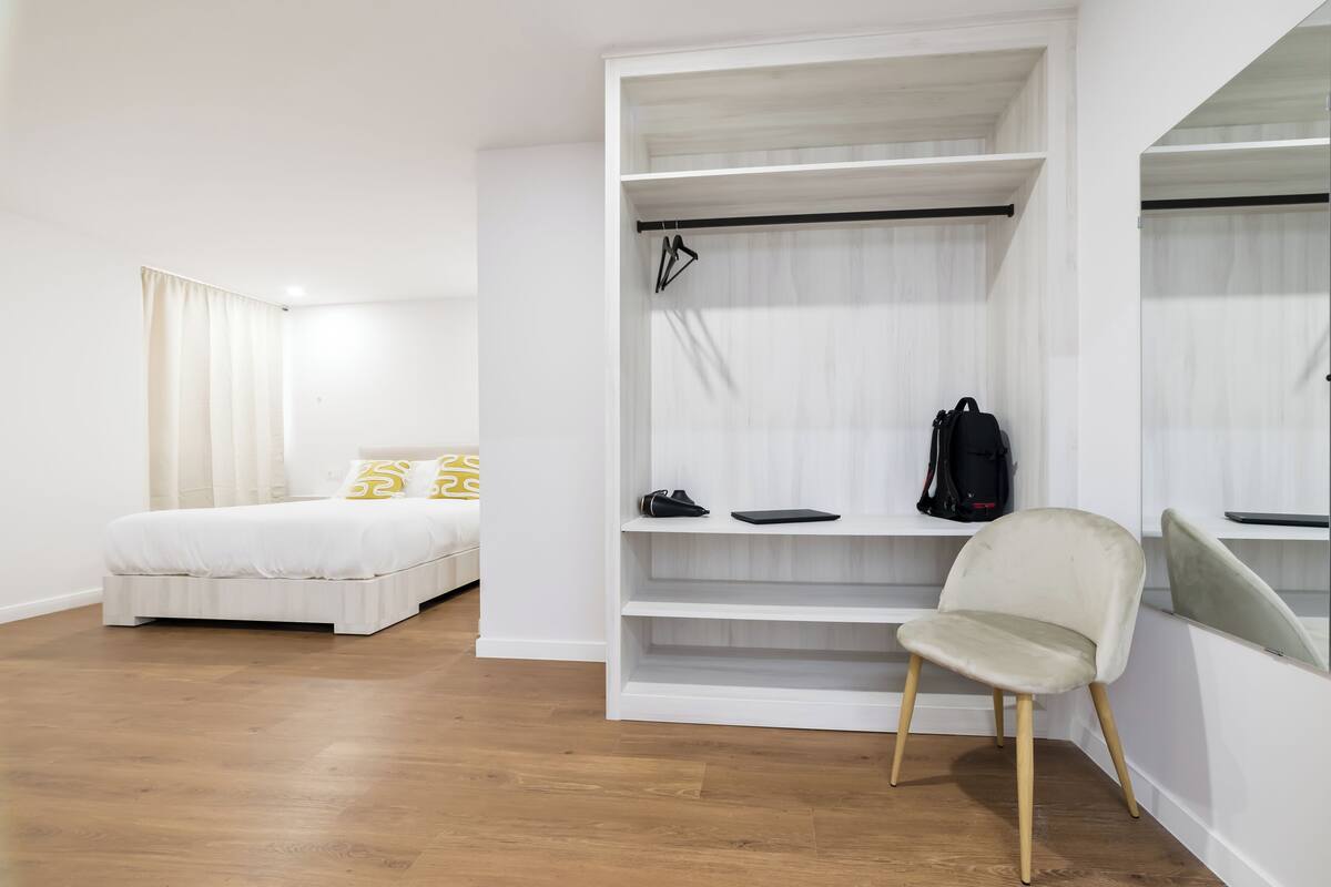 A bedroom with a bed, a white wardrobe, and a chair.
