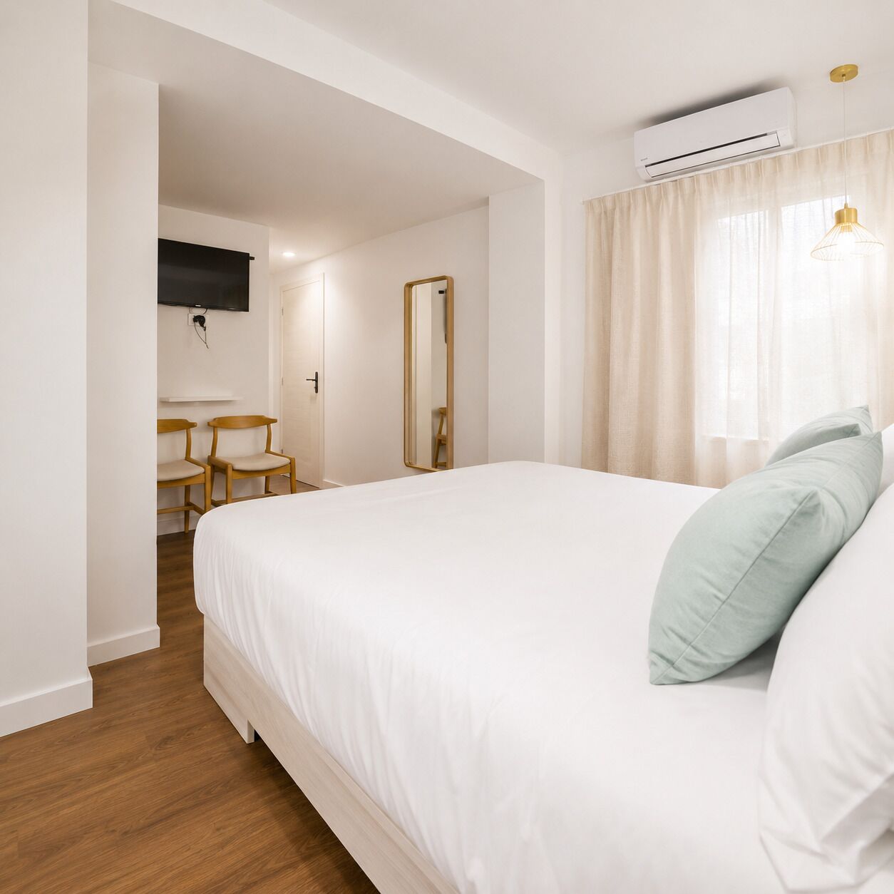 Una habitación de hotel con una cama grande, un televisor de pantalla plana montado en la pared, una silla de madera, un espejo y un equipo de aire acondicionado.