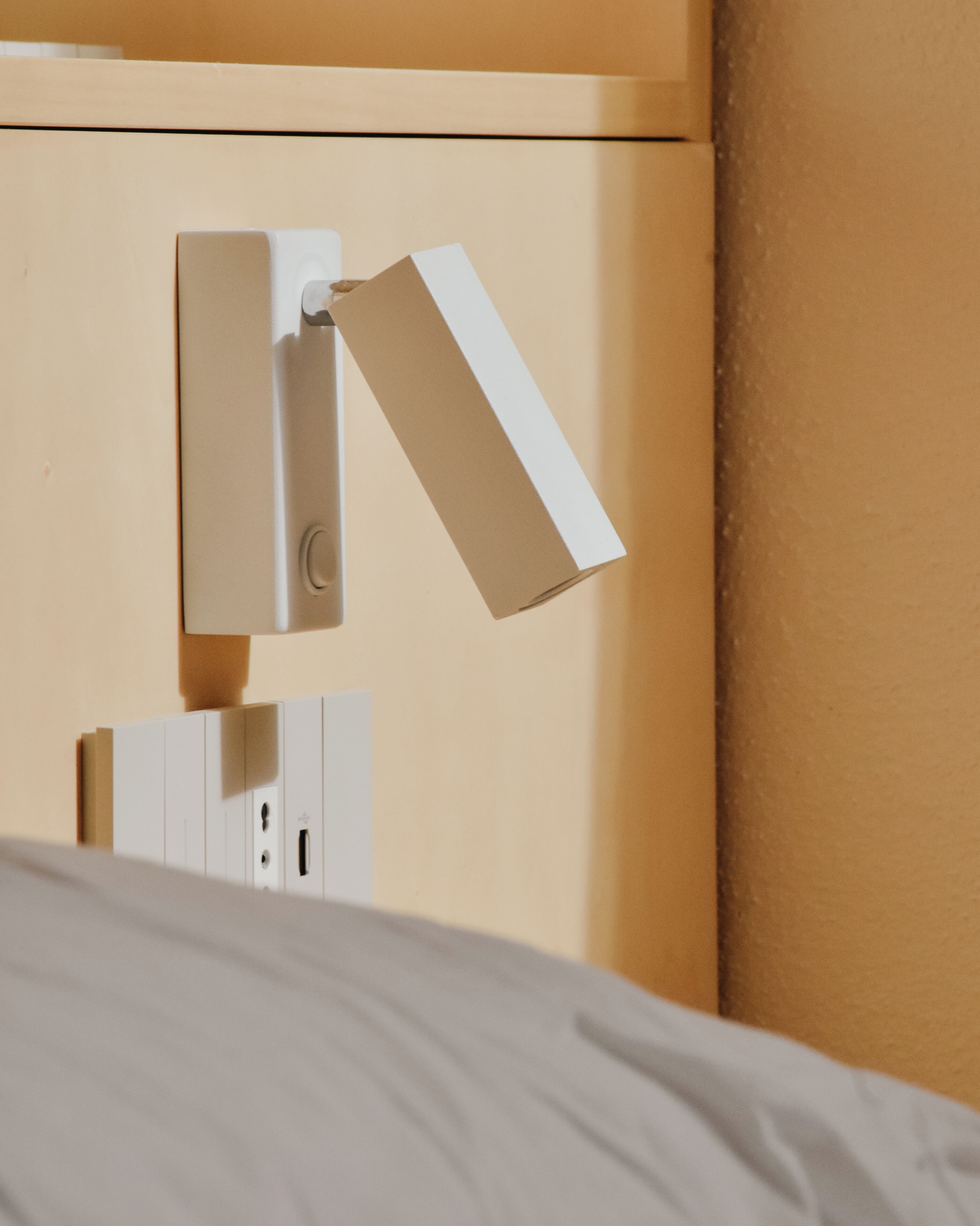 Una cama con cabecera blanca y una lámpara de pared.