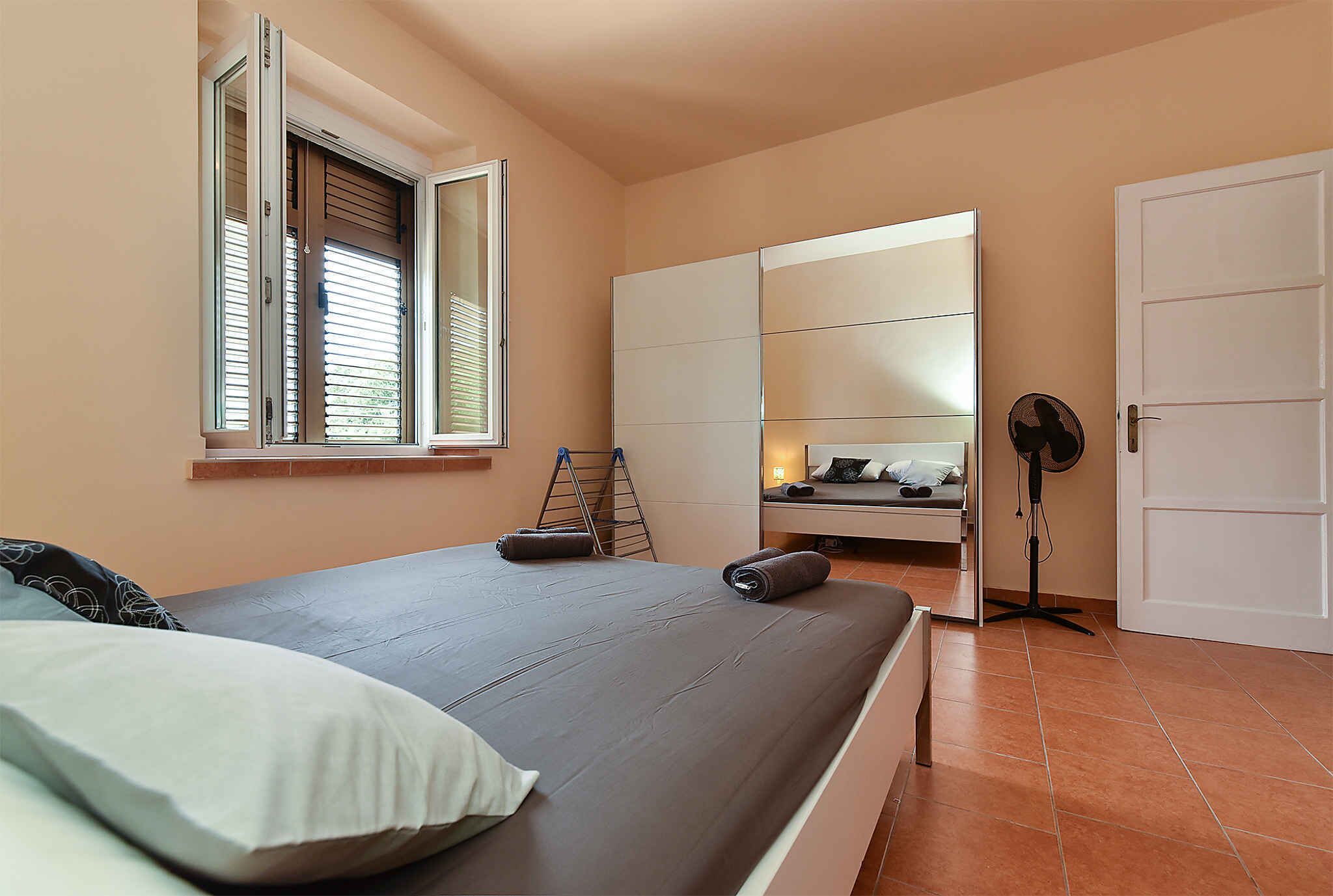 Une chambre à coucher comprenant un lit, une armoire, un bureau et un ventilateur sur pied.