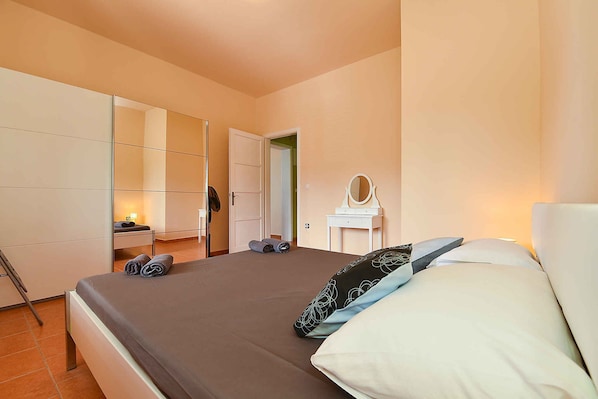 A bedroom with a bed, a bedside table with a mirror, and a wardrobe.