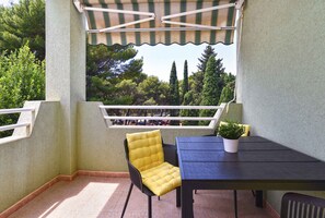 A balcony with a table and chairs, a potted plant, and a view of trees and parked cars. - Holiday apartment with air conditioning (Pula)