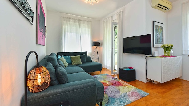 A modern living room with a sectional sofa, a flat-screen TV, a patterned rug, and a ceiling light fixture. - Holiday apartment with air conditioning (Pula)