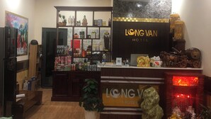 A hotel reception area with a reception desk, a plant, and various items on shelves. - Long Vân Hotel (Phu Quoc)