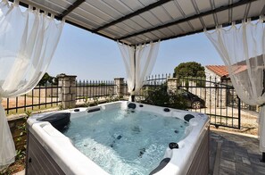 Un bain à remous situé sous une zone abritée, avec vue sur un mur en pierre et une cl ôture.