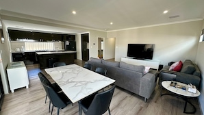A modern apartment with a dining area, a living room with a sofa and TV, and a kitchen.