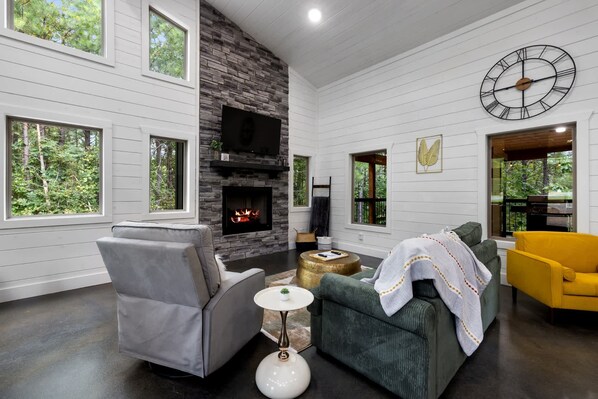 A living room with a stone fireplace, large windows, and a clock on the wall.