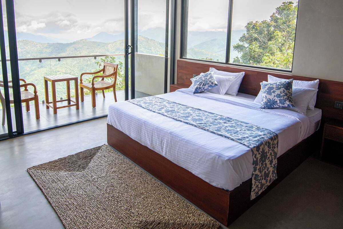 Ein Schlafzimmer mit einem großen Bett, Blick ins Freie und einem Balkon mit Sitzgelegenheiten.
