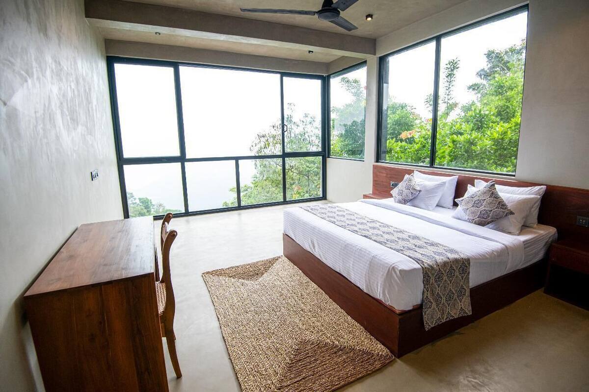 Ein Schlafzimmer mit großem Fenster, einem Bett, einem Schreibtisch und einem Stuhl.