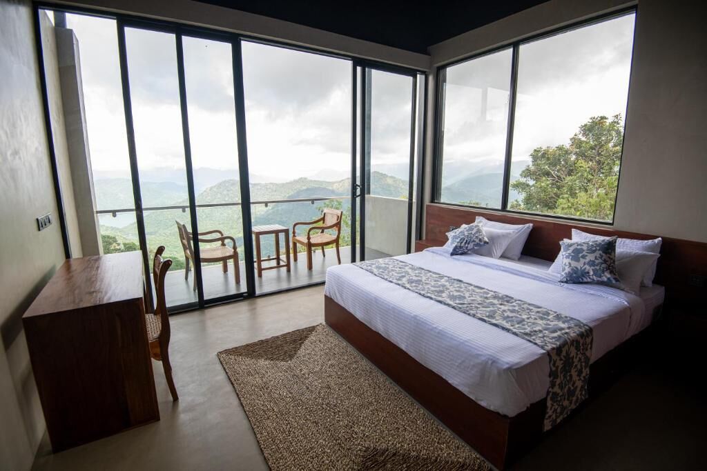 A bedroom with a large bed, a desk, and a chair, with a balcony and a view of the mountains.