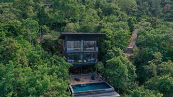 Un bâtiment moderne à deux étages, doté d’une piscine et entouré d’une forêt dense.