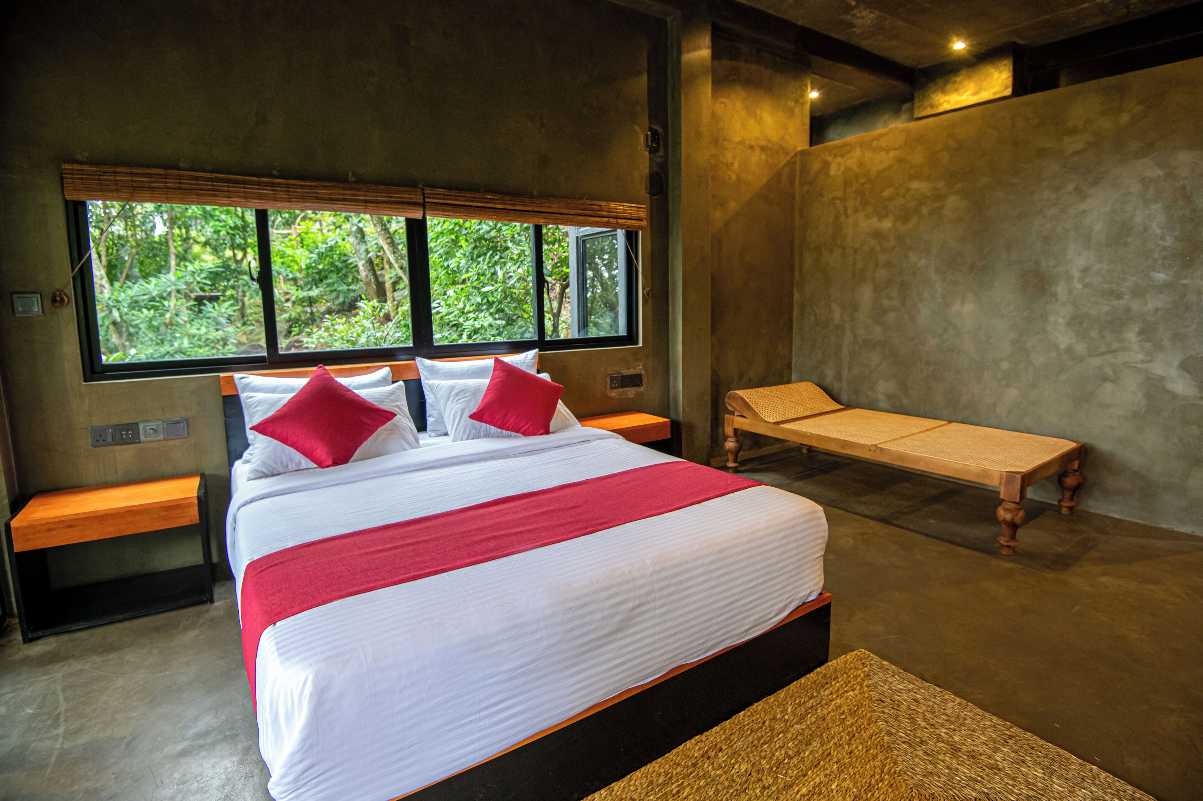 A modern hotel room with a large bed, a bench, and a view of greenery through the window.