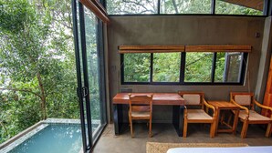 A room with a glass-enclosed pool, wooden furniture, and large windows offering a view of the surrounding greenery. - Nuga Retreat (Illagolla)