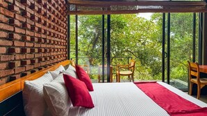 A room with a brick wall, a bed with white and red bedding, and a large window offering a view of trees. - Nuga Retreat (Illagolla)