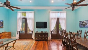 A room with a wooden dining table, chairs, a television, and a ceiling fan.