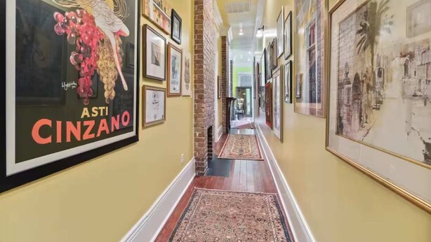 A hallway with framed artwork on the walls, a brick fireplace, and a patterned rug on the floor.