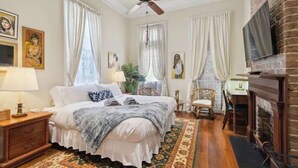 A bedroom with a large bed, a ceiling fan, a fireplace, and a TV mounted on the wall.