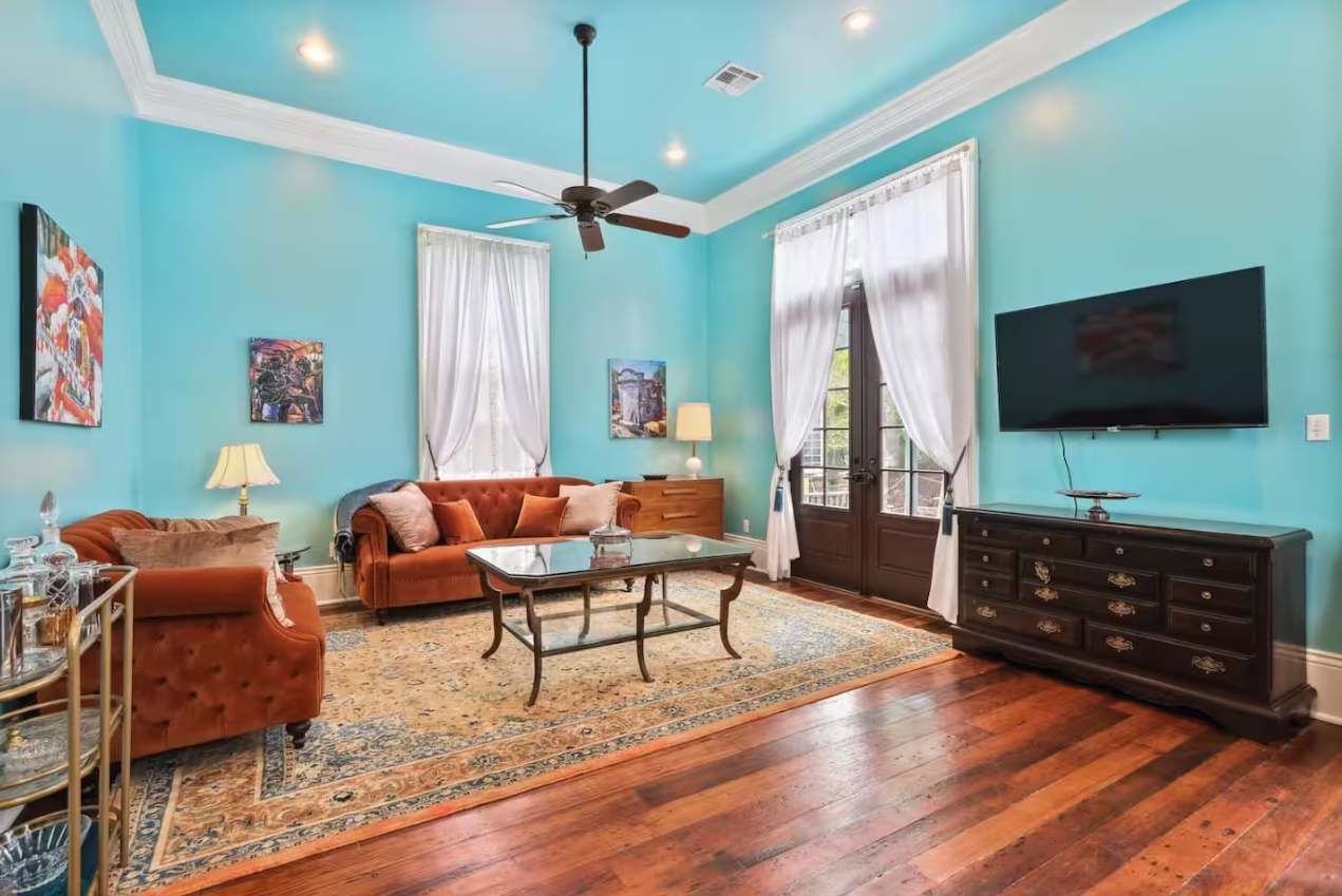A living room with a blue wall, a ceiling fan, a sofa, a coffee table, a TV, and a wooden cabinet.