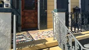 A building entrance with a wooden door, black shutters, and a tiled porch with decorative railings.