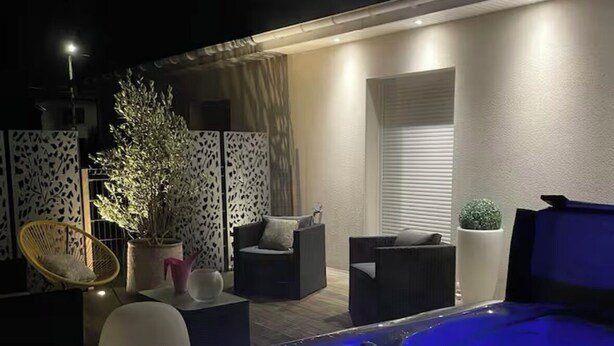 A hot tub with blue lighting, outdoor seating, and a potted plant.