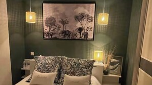 A neatly made bed with patterned pillows, a wall-mounted painting of a natural scene, and two bedside lamps.
