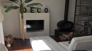 A modern living room with a white sofa, a flat-screen TV, a large potted plant, and a fireplace.