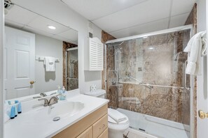 Un bagno moderno con lavandino, specchio e servizi igienici bianchi. Dispone di una doccia con porta in vetro e parete in marmo.