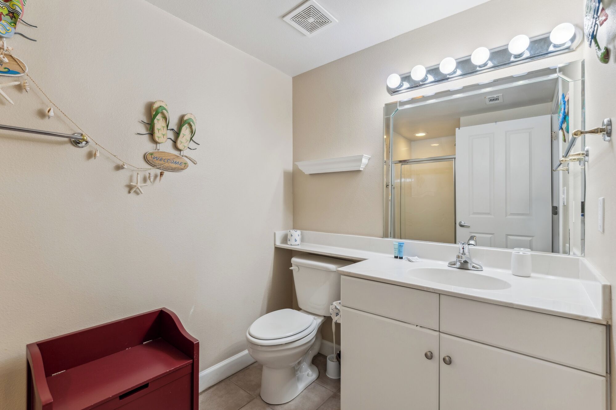 Une salle de bain avec un lavabo blanc, un miroir avec éclairage intégré, des toilettes et un banc rouge.