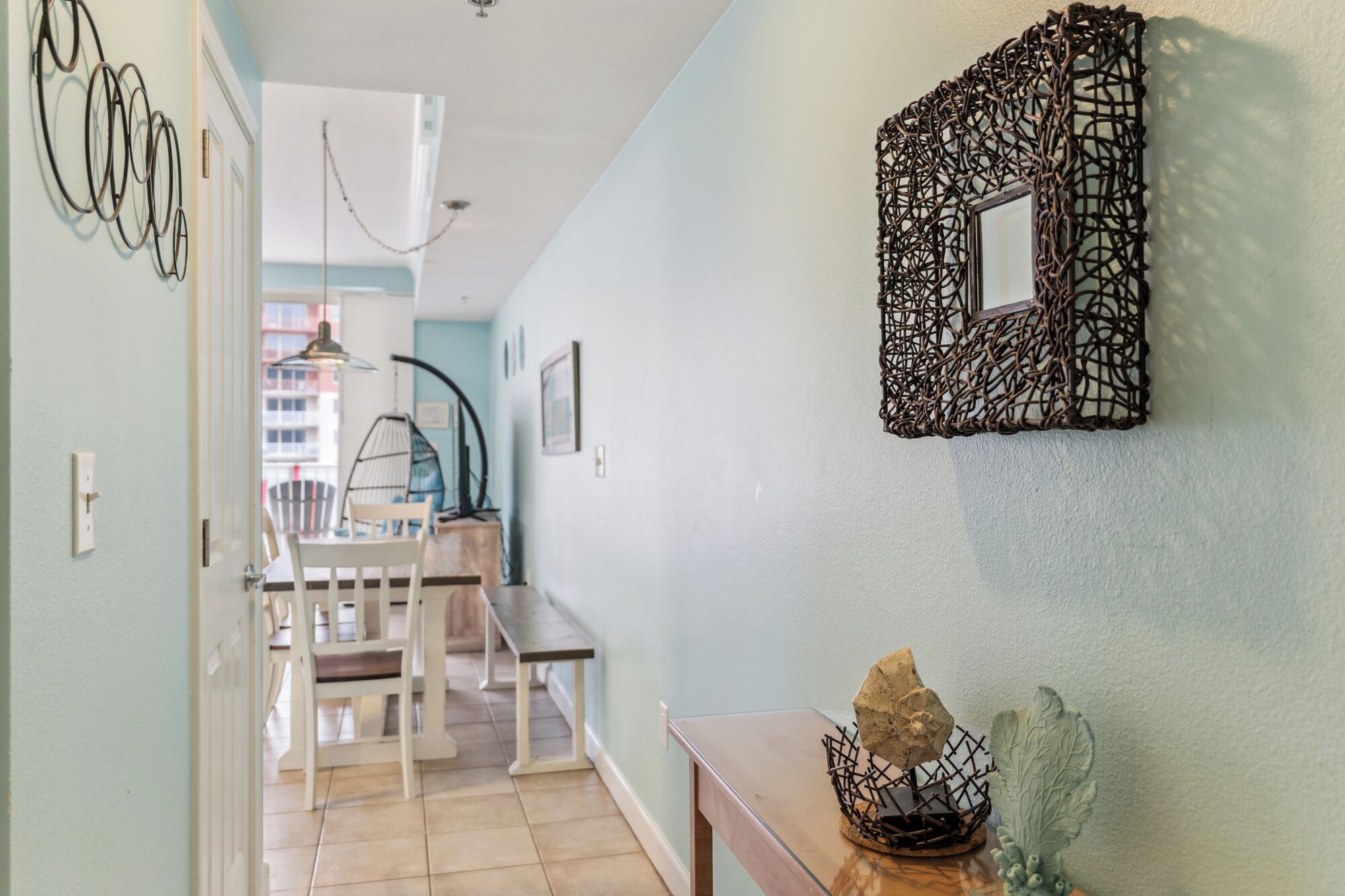 A hallway with a dining area, a wall-mounted decorative mirror, and a small table with a plant.