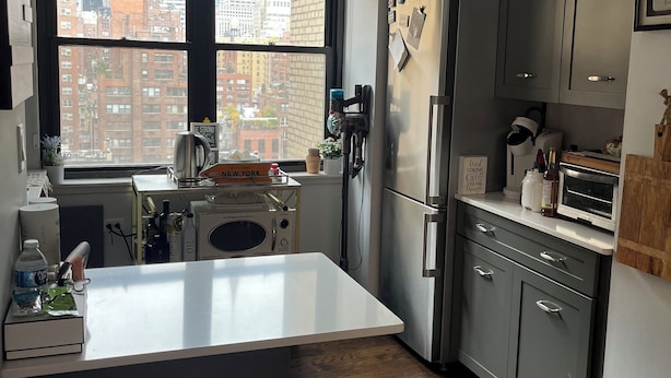 Una cocina moderna con una isla grande, armarios oscuros y vistas de la ciudad a través de un ventanal amplio.