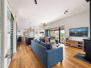 Un salon moderne avec un canapé bleu, un parquet en bois et une grande fenêtre donnant sur l’extérieur.