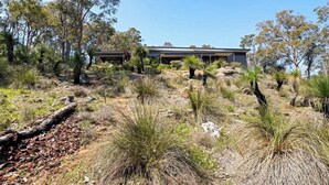 A building with a flat roof and a covered patio area, surrounded by dry grass and sparse trees. - Wildflower Ridge: Elevated Forest & Coastal Escape (Western Australia)