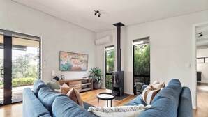 A modern living room with a sofa, a small table, a fireplace, and a painting on the wall. - Wildflower Ridge: Elevated Forest & Coastal Escape (Western Australia)