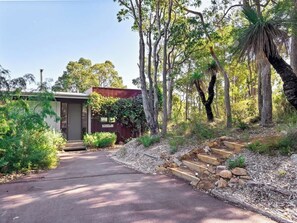 A residential property with a paved driveway leading to a wooden door, surrounded by trees and a small shed.
