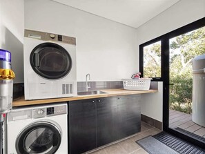 Cocina compacta con lavadora, secadora, lavamanos y ventana con vistas a zonas verdes.
