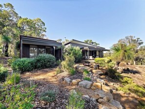 Une maison moderne dotée d’un espace extérieur couvert, entourée de végétation naturelle et de rochers.