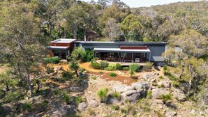 A modern house with a large deck, surrounded by natural vegetation and rocky terrain. - Wildflower Ridge: Elevated Forest & Coastal Escape (Western Australia)