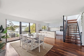 A modern kitchen with a central island, a dining area with a table and chairs, and a staircase leading to an upper level.