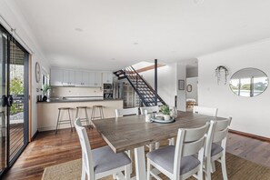 A modern kitchen with white cabinets, a wooden dining table, and a staircase leading to an upper level.