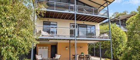 Un bâtiment à deux étages doté d’un balcon, d’un espace extérieur aménagé pour s’asseoir et offrant une vue sur la verdure environnante.