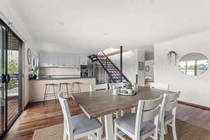 Una cocina moderna con armarios blancos, una mesa de comedor de madera y una escalera que conduce a un nivel superior.