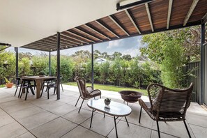 En udendørs terrasse med et bord og stole, et bålsted og en pergola.