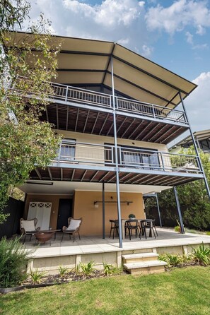 A multi-level residential building with a covered patio area, outdoor seating, and a staircase leading to the entrance.