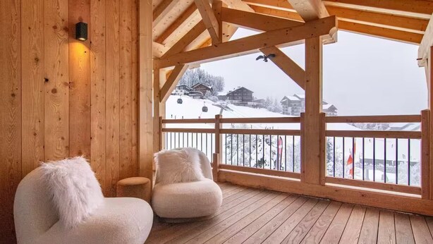 Una terraza de madera con dos sillones cómodos y una mesita, con vista a un paisaje montañoso nevado.