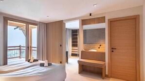 Un dormitorio moderno con una cama grande, una banca, una puerta de madera y vistas a un balcón.