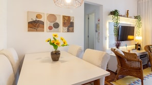 Ein modernes Wohnzimmer mit einem weißen Esstisch, Korbstühlen und einem Fernseher auf einem Schrank.